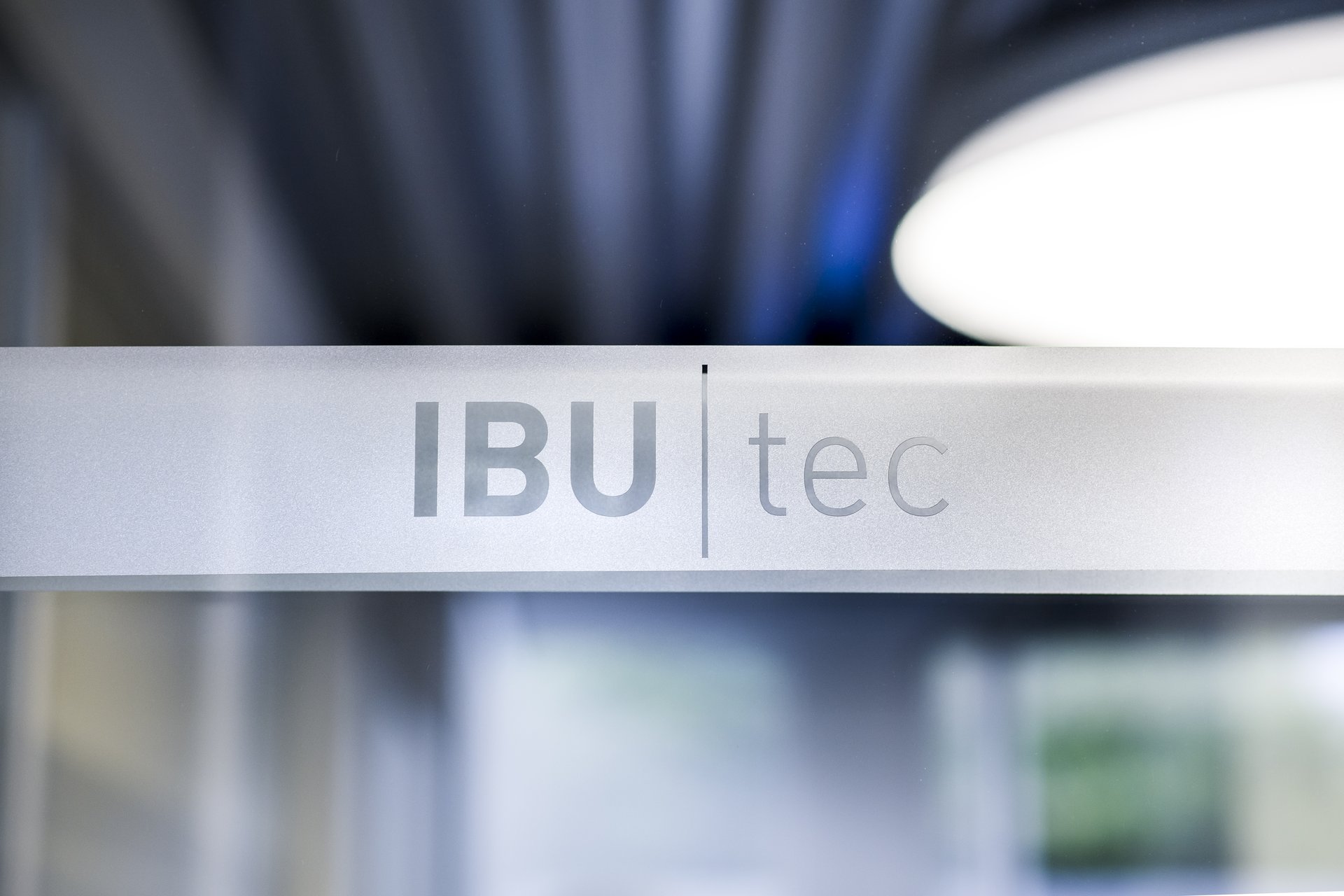 IBU-tec Logo with beautiful artsy lights in the background: blue, grey and white. Some green